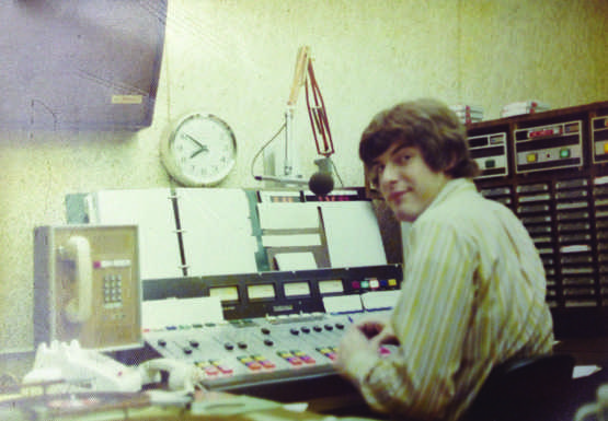 Associate Communication professor Tom McCray sitting at an old soundboard mixing studio.