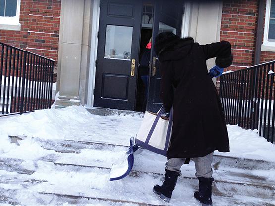 A faculty member shovels snow off the stoop outside Ketchem Hall.